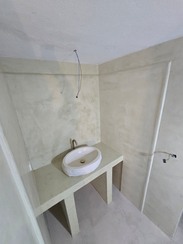 Minimalist bathroom interior with white round vessel sink on concrete countertop, bare walls, and ceiling-mounted fixtures