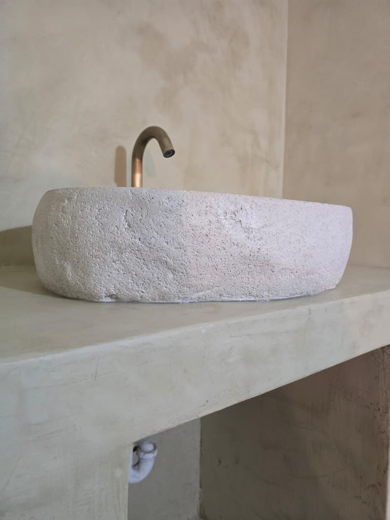 White textured stone vessel sink with bronze curved faucet on minimal white bathroom counter