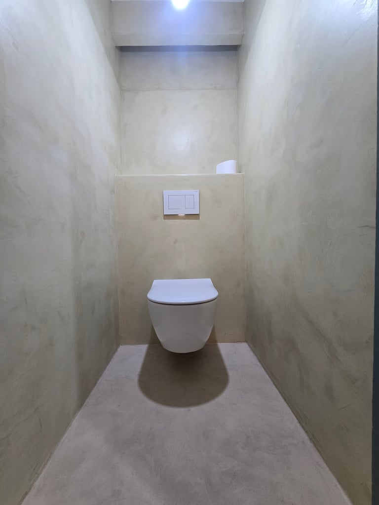 Minimalist modern bathroom with white wall-mounted toilet in narrow beige-tiled stall with recessed lighting